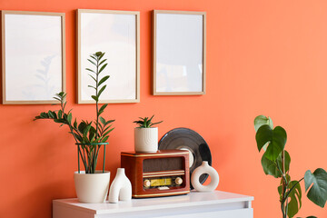 Retro radio, vinyl disk and houseplants on white dresser near orange wall