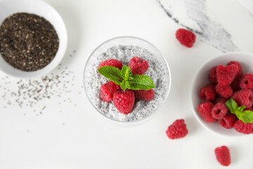 Glass of tasty chia seed pudding with fresh raspberries and mint on white background