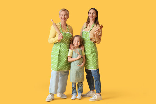 Happy family in aprons with cooking utensils on yellow background