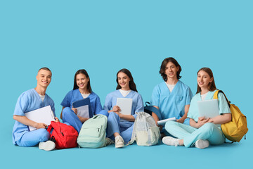 Group of medical students with laptops and backpacks sitting on blue background