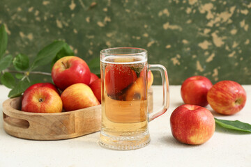 Glass cup of fresh apple cider and wooden tray with fruits on white table