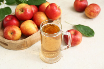 Glass cup of fresh apple cider and wooden tray with fruits on white background