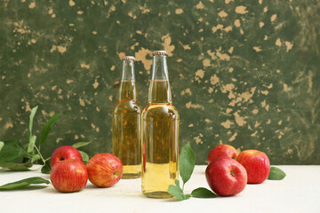 Bottles of fresh apple cider and fruits on white table