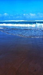 Waves crashing on a dark, black sand beach with foam and the blue ocean.