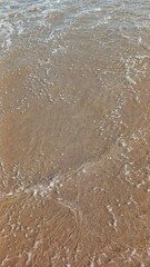 A close-up of a sandy beach with gentle waves and seafoam.