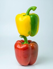 Two bell peppers, yellow and green atop a red one, balanced vertically against a plain background