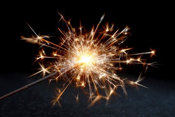 Fototapeta premium A bright sparkler emits golden sparks against a dark background
