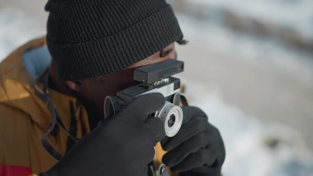 high angle view of professional photographer peering through viewfinder of vintage camera, gloved hand adjusting lens dial and pressing shutter for precise focus under bright winter sunshine