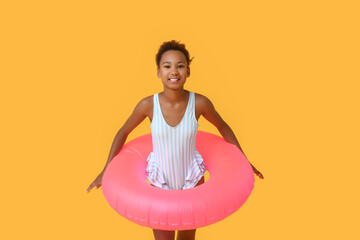 Cute little African-American girl in swimsuit with inflatable ring on yellow background