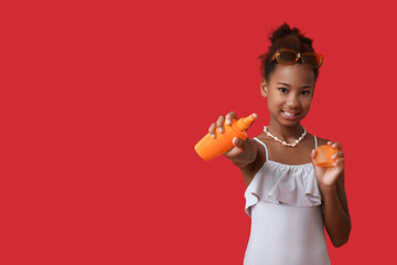 Cute little African-American girl in swimsuit with sunscreen cream on red background