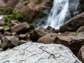 Cracked stone foreground with blurred waterfall and rocky landscape background