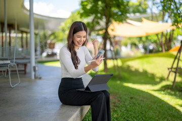 Excited businesswoman celebrating success while using tablet and smartphone outdoors