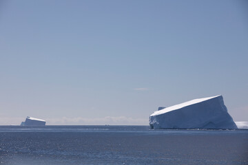 Two massive icebergs floating in the open ocean near Antarctica under clear blue sky