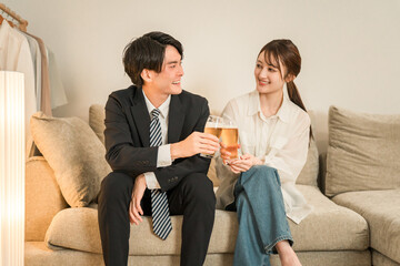 夜,帰宅後にソファに座りながらビールを飲む若いアジア人夫婦,カップル

