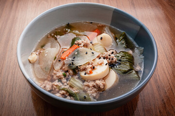 Clear soup with tofu, egg, minced pork, cabbage, carrots, onions, and sprinkled with black and white sesame seeds.