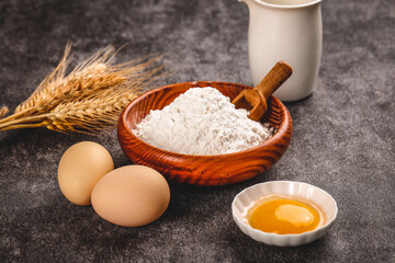 Fresh wheat flour in wooden bowl with eggs and milk - baking ingredients for homemade bread and pastry making
