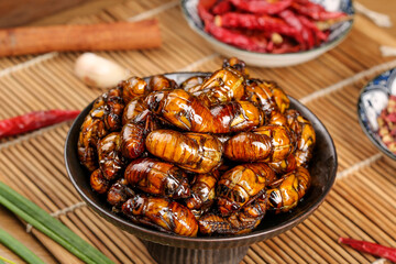 Fried Silkworm Pupae in Bowl - Traditional Asian Street Food Delicacy on Bamboo Mat