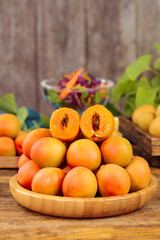Fresh Organic Apricots in Wooden Bowl with Cut Half Showing Pit on Rustic Kitchen Table