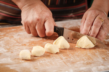 Baker cutting freshly kneaded wheat dough portions on flour-dusted wooden cutting board for homemade bread making