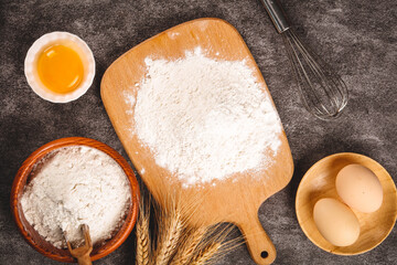 Fresh wheat flour and baking ingredients on wooden cutting board with eggs and grains for homemade bread preparation