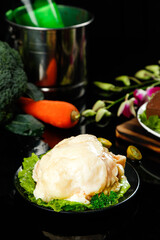 Raw whole chicken with fresh vegetables and cooking preparation setup on dark kitchen counter