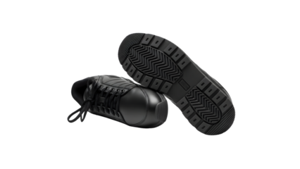 A pair of black leather sneakers with laces and a textured sole on a dark background in a studio shot