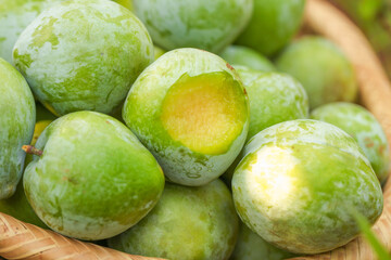 Freshly Picked Green Plums in Wooden Basket with Cut Open Fruit Showing Golden Flesh