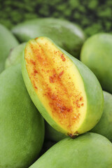 Freshly picked raw green Hainan mango with spice seasoning cut in half among whole tropical fruits