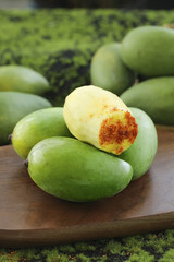 Fresh Green Hainan Mangoes with Cut Open Fruit Showing Ivory Flesh on Wooden Board