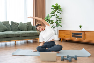 Young Asian woman stretching yoga workout on exercise mat while online training class with computer...
