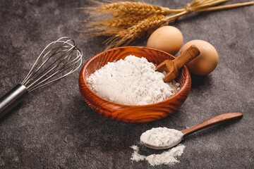 Fresh flour and baking ingredients with wheat stalks and eggs on dark stone surface for homemade bread making