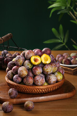 Freshly Picked Ripe Plums in Wicker Basket with Cut Halves Showing Red Yellow Flesh on Wood Table
