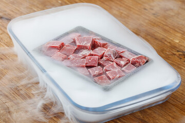 Fresh Raw Diced Beef Cuts in Vacuum Container with Dry Ice Smoke Effect on Wood Background