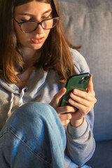 Vertical Close up of teen girl relaxing with her phone a in cozy living room. 