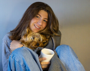 Smiling young woman with her little dog in the living room drinking coffee.