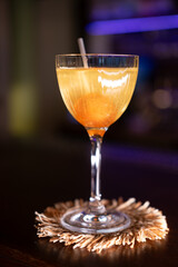 Cocktail served. Pub order. Glass with yellow liquor standing on exotic coaster straw mat. Sweet alcoholic beverage with candy lollipop.