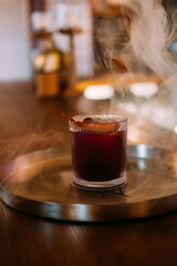 Served liquor. Alcoholic beverage. Aromatic smoke negroni on metal tray. Scented cold cocktail presentation on restaurant bar counter.