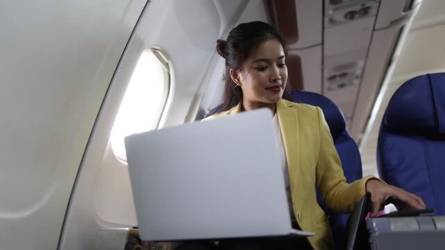 Businesswoman working on laptop during flight, sitting comfortably near airplane window during business travel.