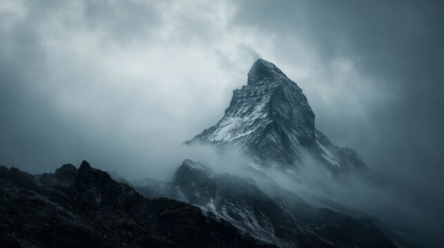 Dark atmospheric surreal landscape with towering rocky mountain peak covered in snow and surrounded by low gray clouds in gloomy overcast sky creating a mysterious and dramatic surrealist wilderness s