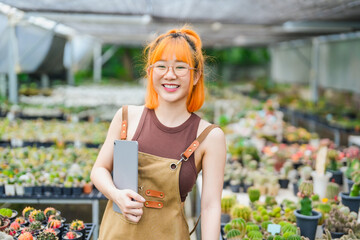 Young Asian Woman Working in Greenhouse Tree Farm as Eco Business Owner with Tablet in Cactus Shop