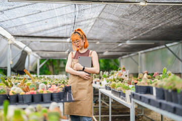 Young Asian Woman Working in Greenhouse Tree Farm as Eco Business Owner with Tablet in Cactus Shop