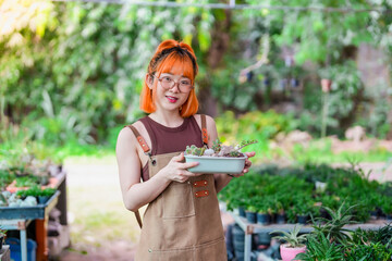 Asian Female Gardener Potting Houseplants in Greenhouse Surrounded by Plants and Pots at Her Loving...