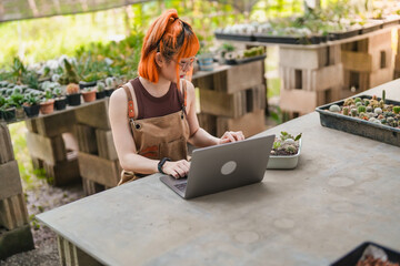 Happy Asian Woman Small Business Owner Working on Laptop at Cactus Eco friendly market store.