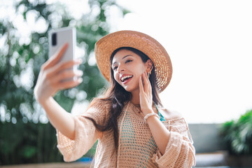 Young Hispanic Gen Z Woman Using Smartphone to Update Social Media by Resort Pool During Summer...