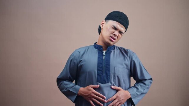 Young Muslim man experiencing stomach pain clutching abdomen with pained expression