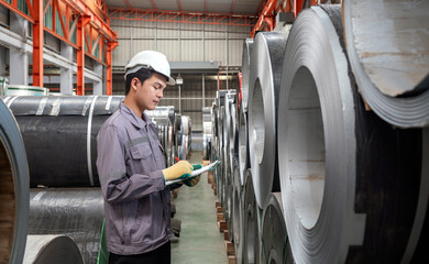 A worker dressed in hardhat and  protective glove, stand in a factory check material while holding...