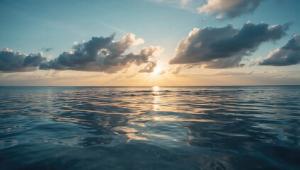 Obraz premium Serene ocean view at sunset with calm waves reflecting golden light and soft clouds