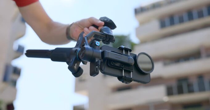 Close-up of hand operating FeiyuTech Scorp Mini gimbal with smartphone. Vlogger or content creator filming outdoors. For technology or social media content
