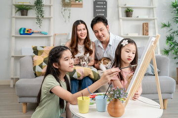 Obraz premium Asian young daughters enjoy painting on board with their parents at home. 