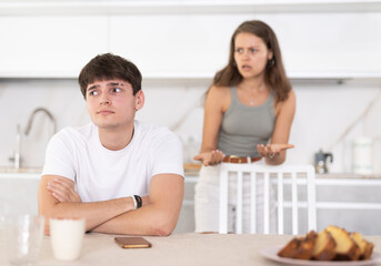 Young woman quarrels with young guy in kitchen at home